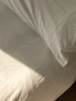 Bright natural sunlight illuminating a perfectly made luxury bed with crisp white linens and a bronze bedside lamp.