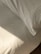 A neatly made bed with white sheets and a pillow is bathed in soft, natural light. The fabric has a slight texture and wrinkles, hinting at the presence of sunlight casting subtle shadows.