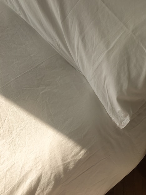 A neatly made bed with soft, inviting sheets and pillows in a sunlit bedroom.