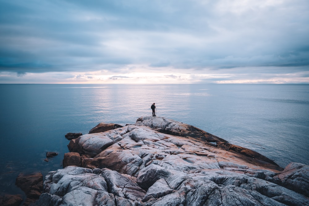 person standing on rock formation near body of water during daytime