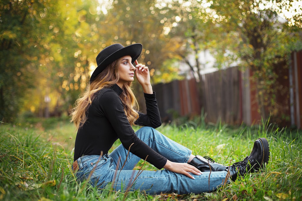 Donna in camicia nera a maniche lunghe e jeans di jeans blu seduta sull'erba verde durante il giorno