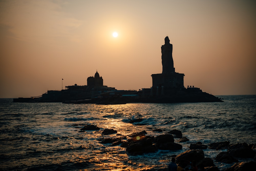 silhouette of building on rock formation near body of water during sunset