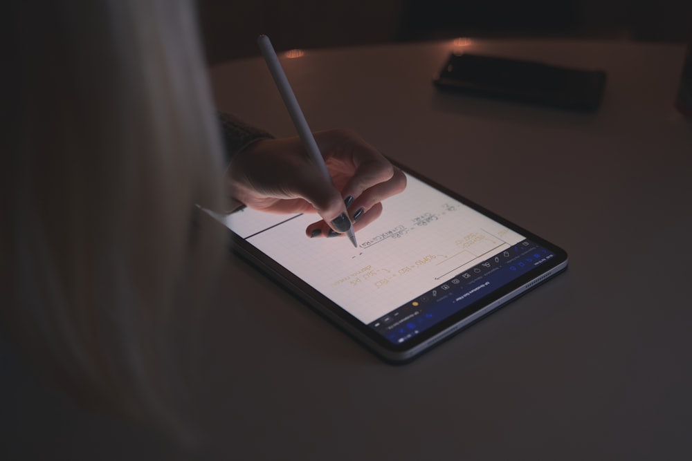 Someone using an Apple iPad with an Apple pencil on a white table in a dark room