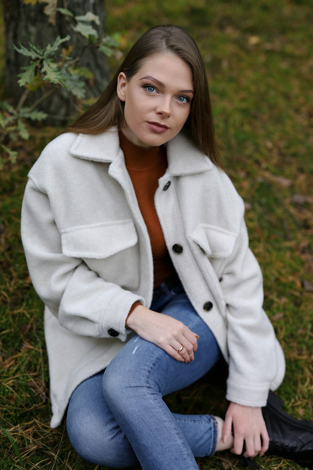woman in white coat and blue denim jeans sitting on green grass during daytime