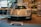 A sleek, high-performance sports car is displayed in a showroom with other luxury vehicles. The car features aerodynamic curves and distinctive headlights. The setting includes a stylish interior with art and photographs on the walls.