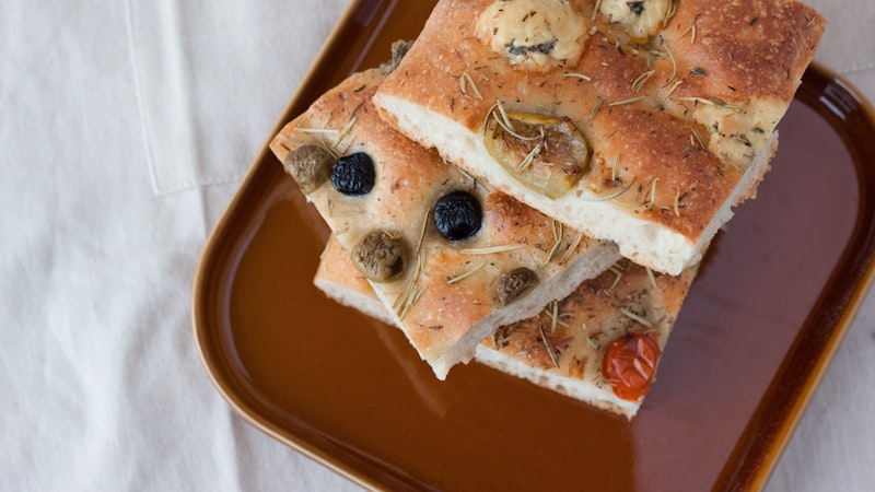 Slices of olive topped flatbread on a terracotta plate