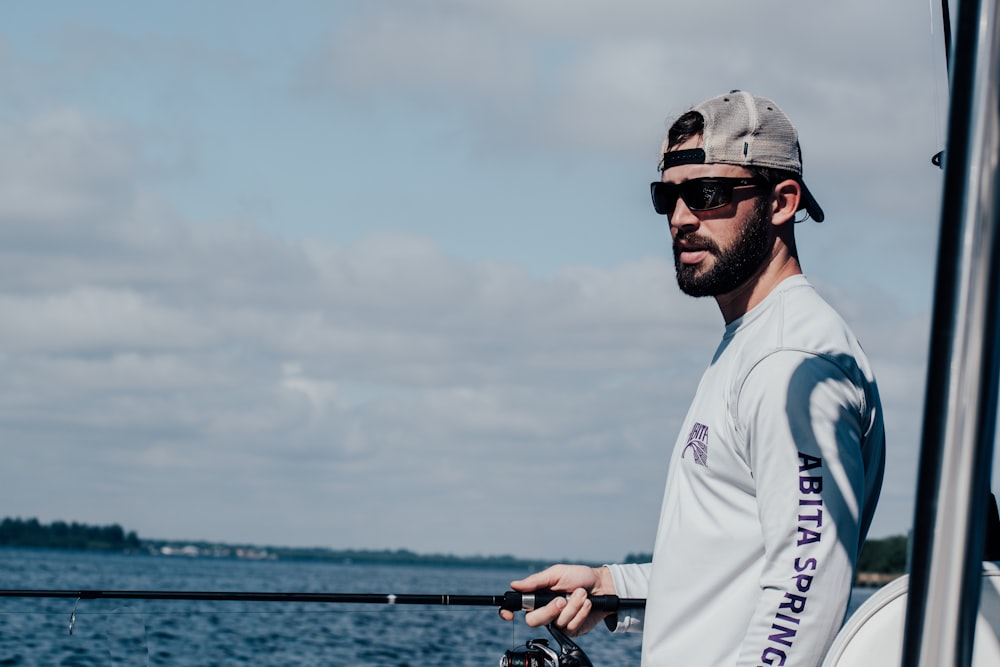 man in white crew neck t-shirt wearing black sunglasses holding black fishing rod during daytime