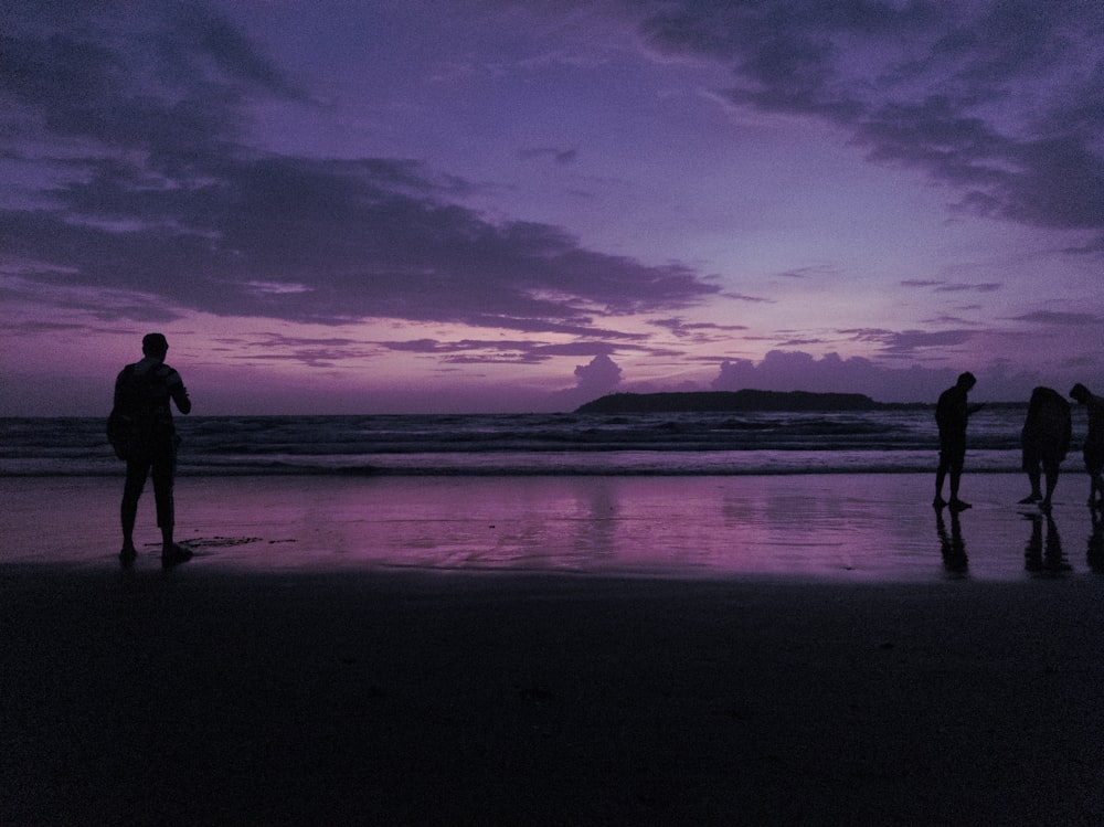 Silueta del hombre y de la mujer de pie en la orilla del mar durante la puesta del sol