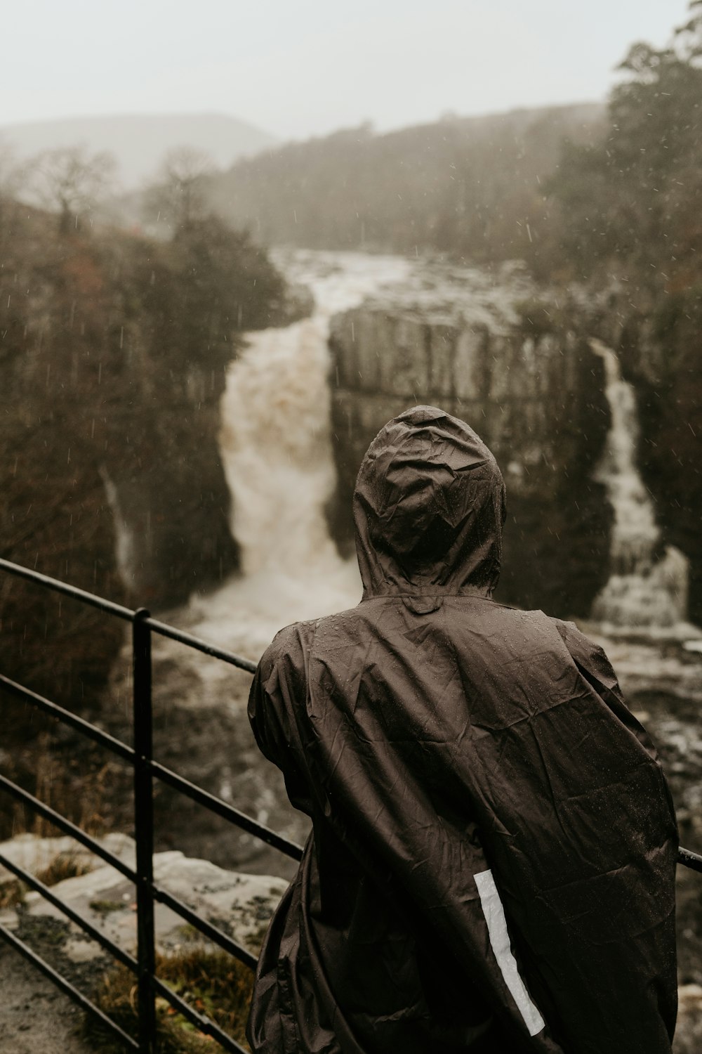 grayscale photo of man in jacket standing on bridge