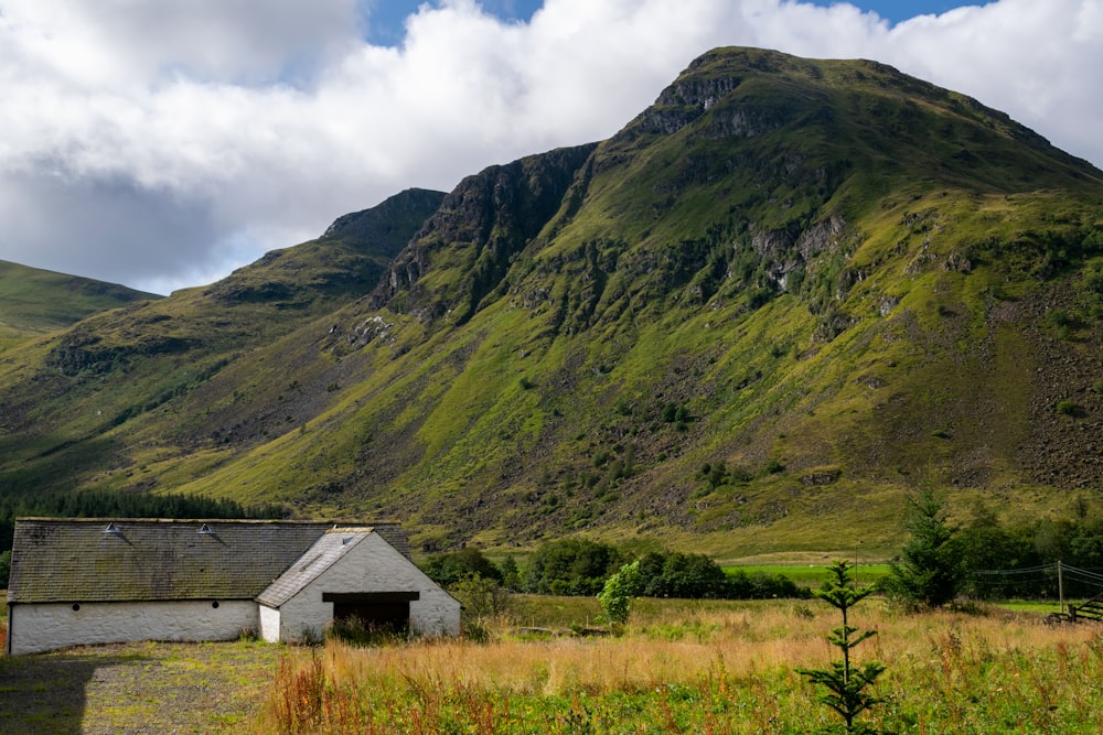 white wooden house on green grass field near mountain under white clouds during daytime