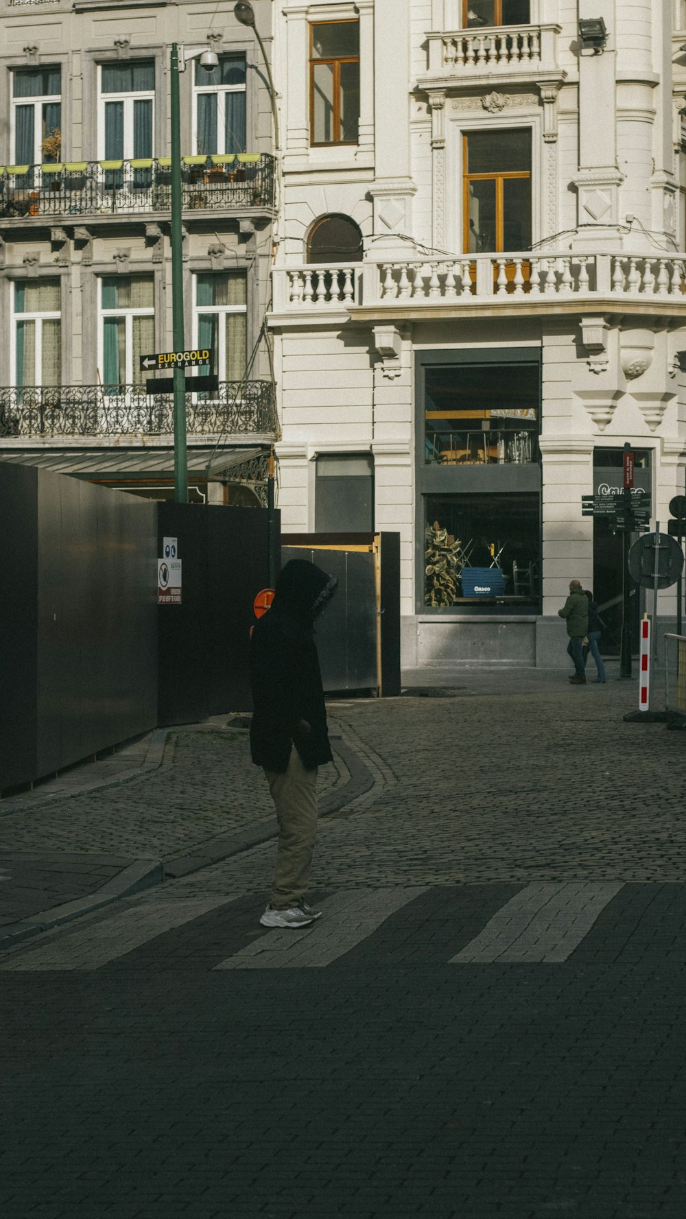 homme en veste noire et pantalon gris marchant sur le trottoir pendant la journée