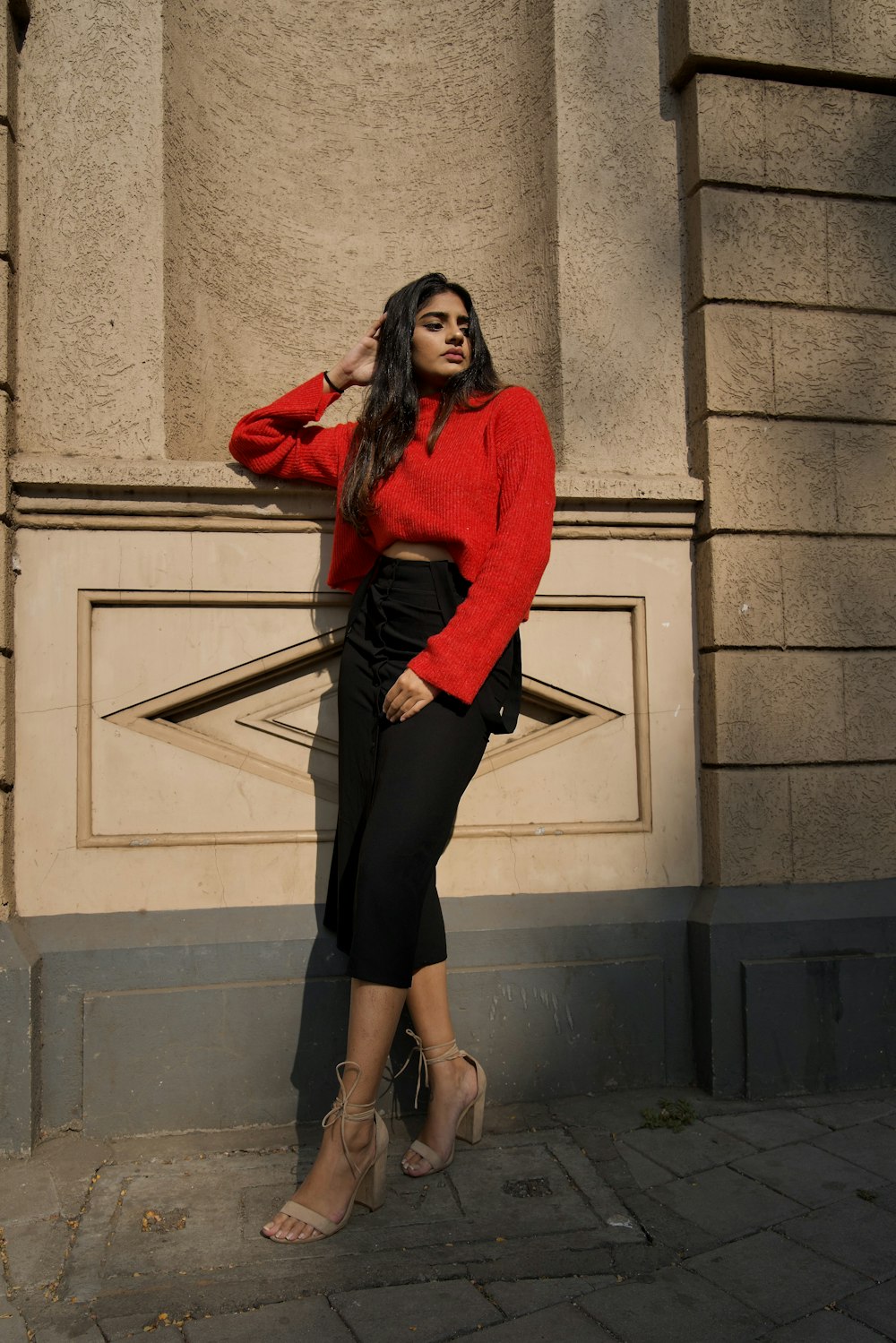 woman in red long sleeve shirt and black skirt standing beside gray concrete wall