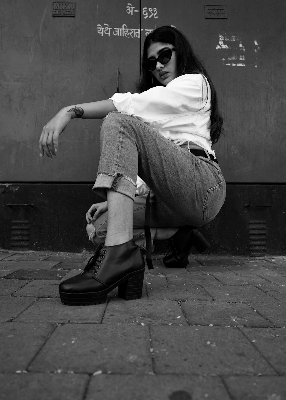 woman in white shirt and gray denim jeans sitting on concrete wall