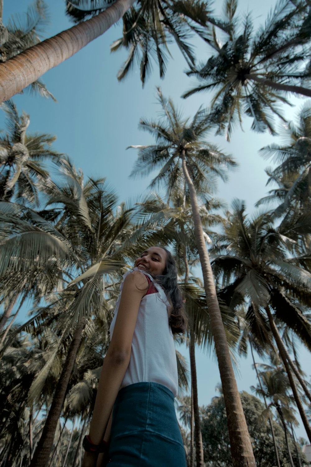 femme en robe blanche sans manches debout près d’un palmier pendant la journée