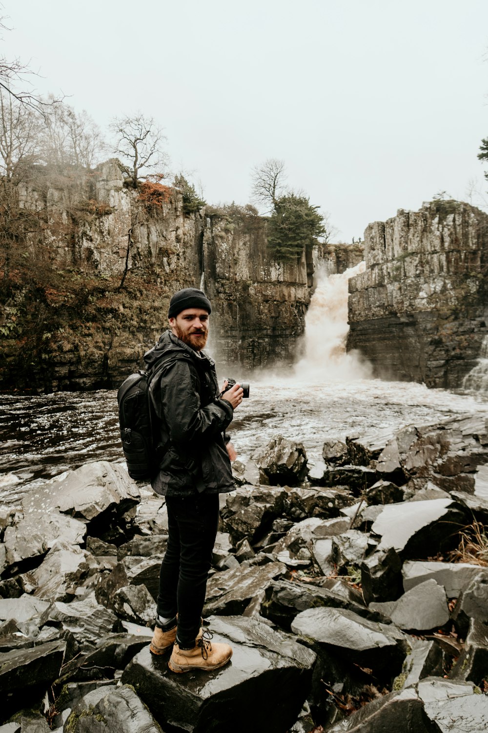 man in black jacket standing near waterfalls during daytime