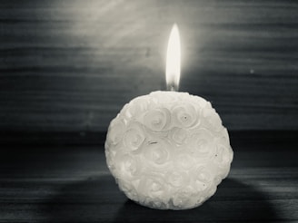 A softly glowing Silk Trade Candle nestled among delicate rose petals on a dark, elegant background.