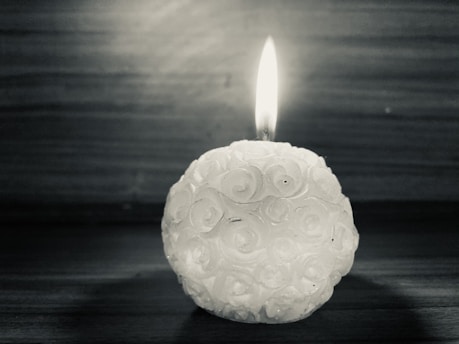 A softly glowing Silk Trade Candle nestled among delicate rose petals on a dark, elegant background.