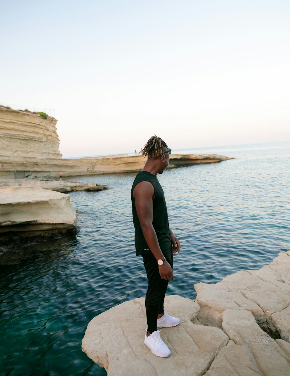 woman in black tank top and black pants standing on rock near body of water during