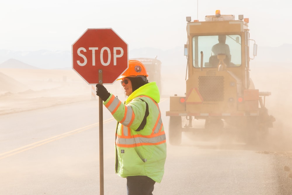 man in green and yellow jacket holding stop sign