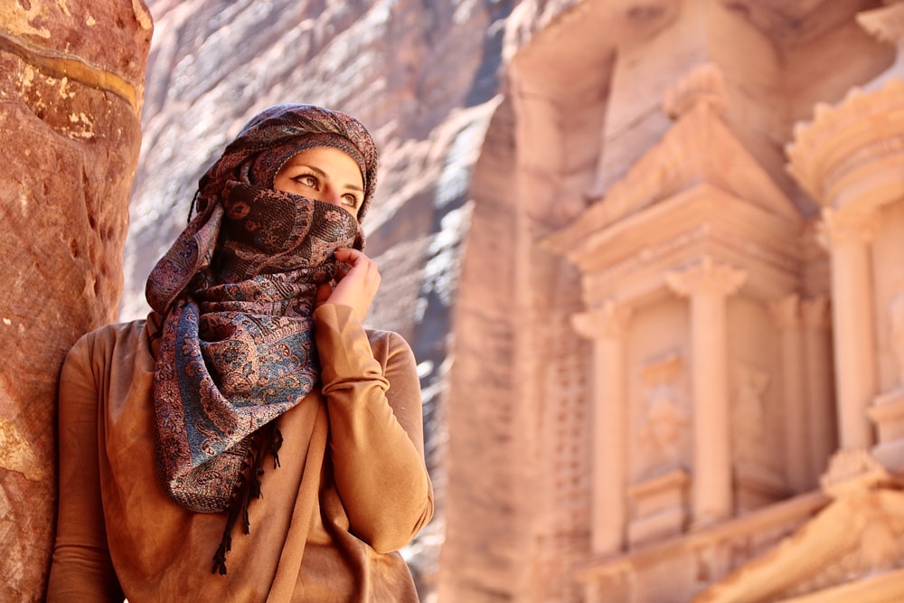 femme en hijab brun debout près d’un bâtiment en béton brun pendant la journée