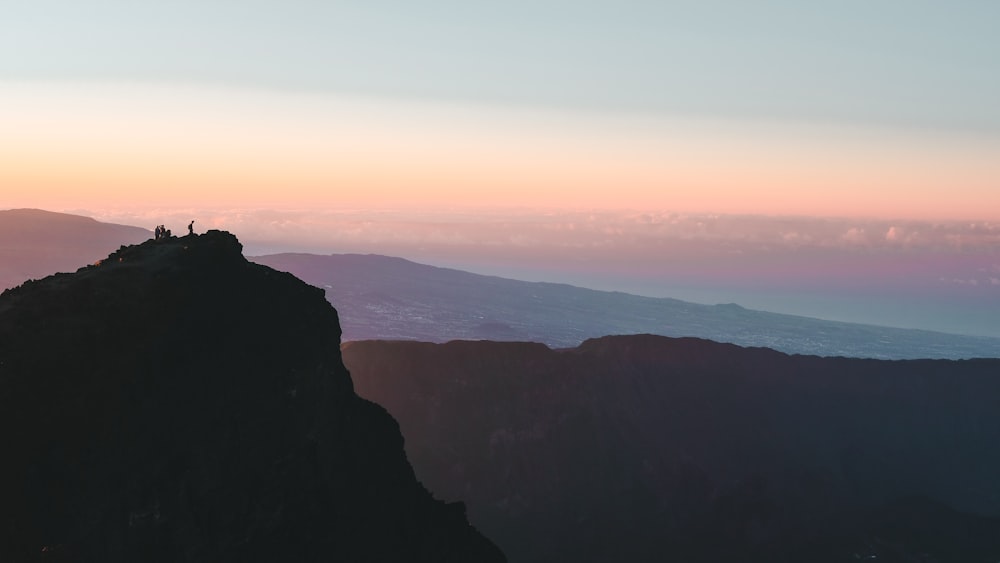 silhouette of person standing on rock formation during sunset