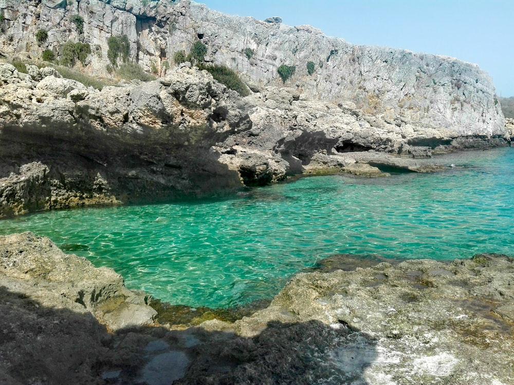 body of water near gray rocky mountain during daytime