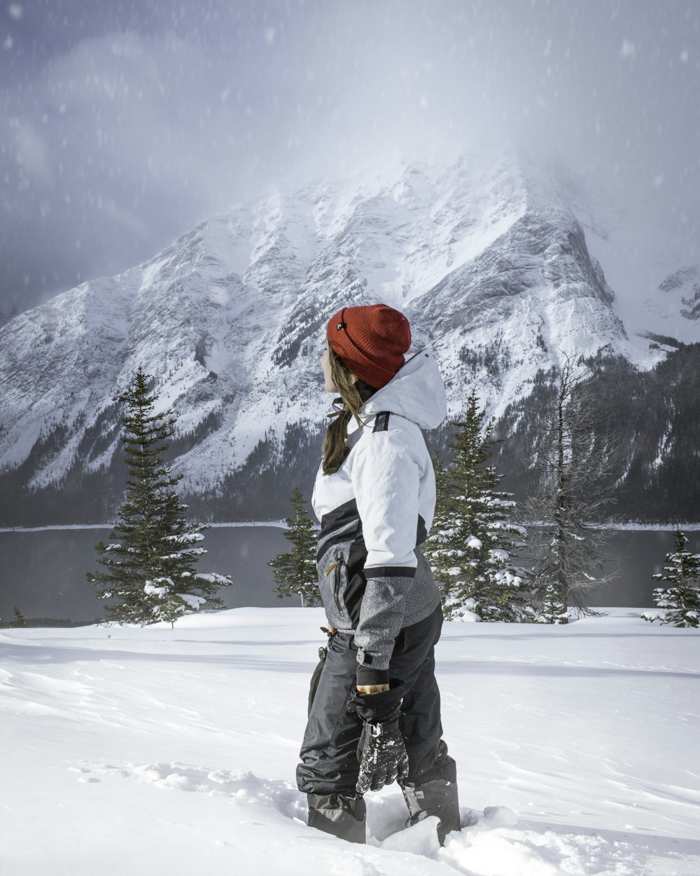 woman in white jacket and red knit cap standing on snow covered ground
