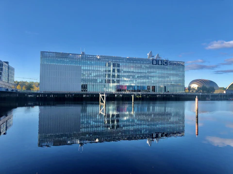 A sleek glass office building reflecting the nearby river under a clear sky.