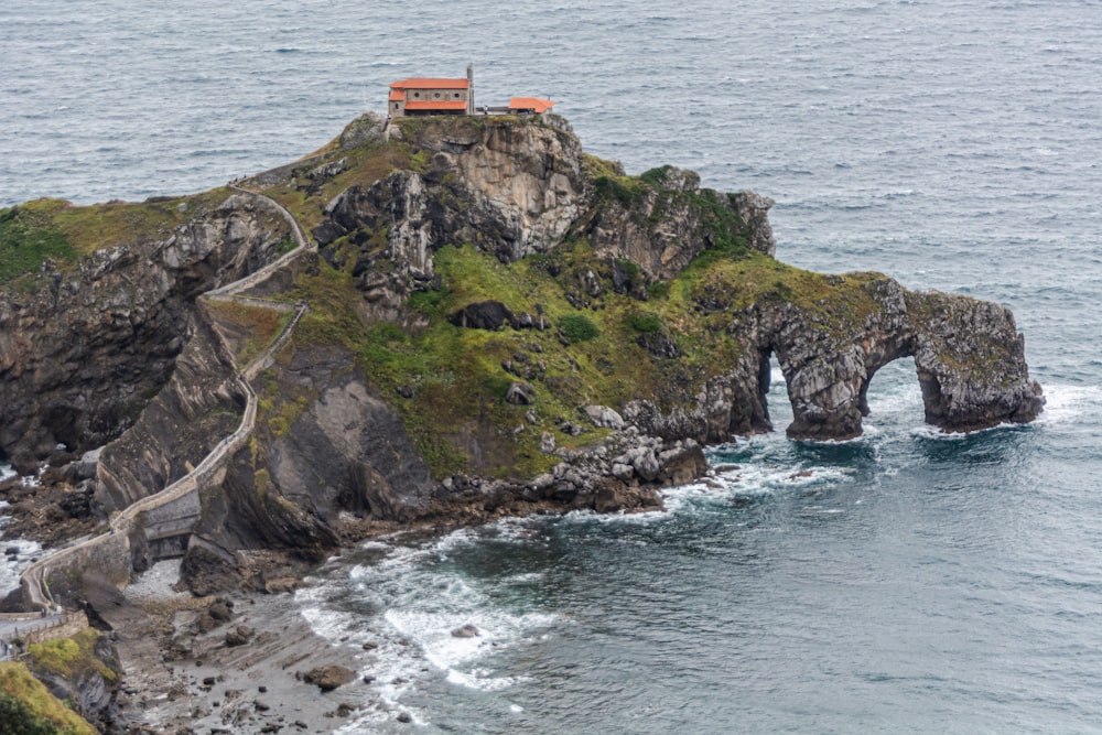 orange and white house on green and brown rock formation beside sea during daytime