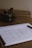 A spiral-bound sketchbook lies open on a brown surface, displaying a pencil outline of the word 'THINK' in large block letters. A pencil rests beside the notebook. To the left, there is a small plant with dark green leaves partially blurred in the background.