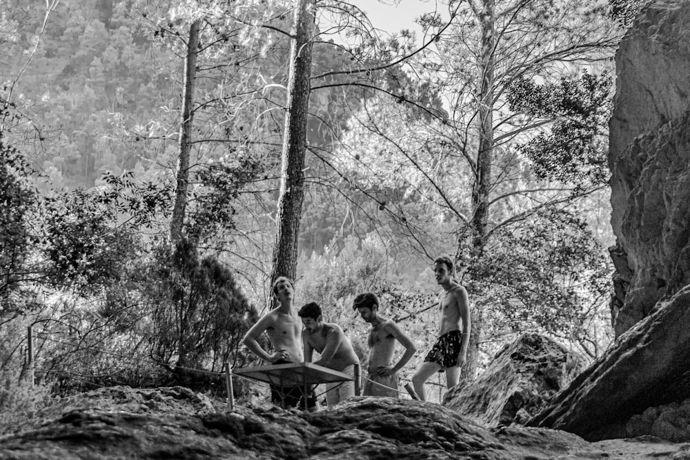 grayscale photo of 3 men sitting on tree log