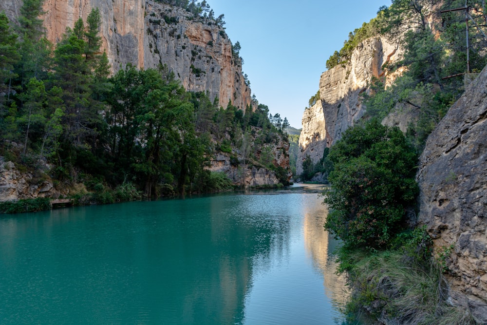 green lake surrounded by green trees and brown rocky mountain under blue sky during daytime