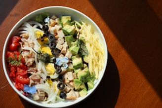 Close-up of a colorful bowl of Mexican-style salad with avocado, beans, corn, and grilled chicken.