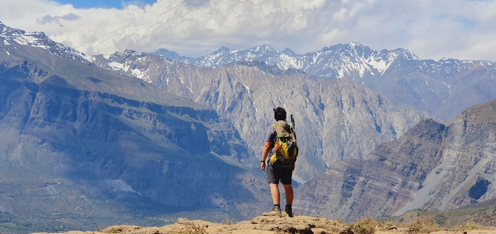 Uomo in zaino nero in piedi sulla montagna rocciosa marrone durante il giorno
