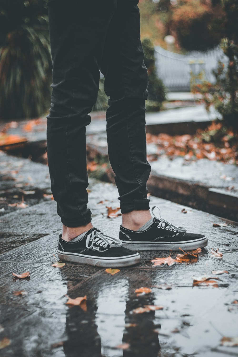 person in black pants and black and white nike sneakers standing on gray concrete pavement