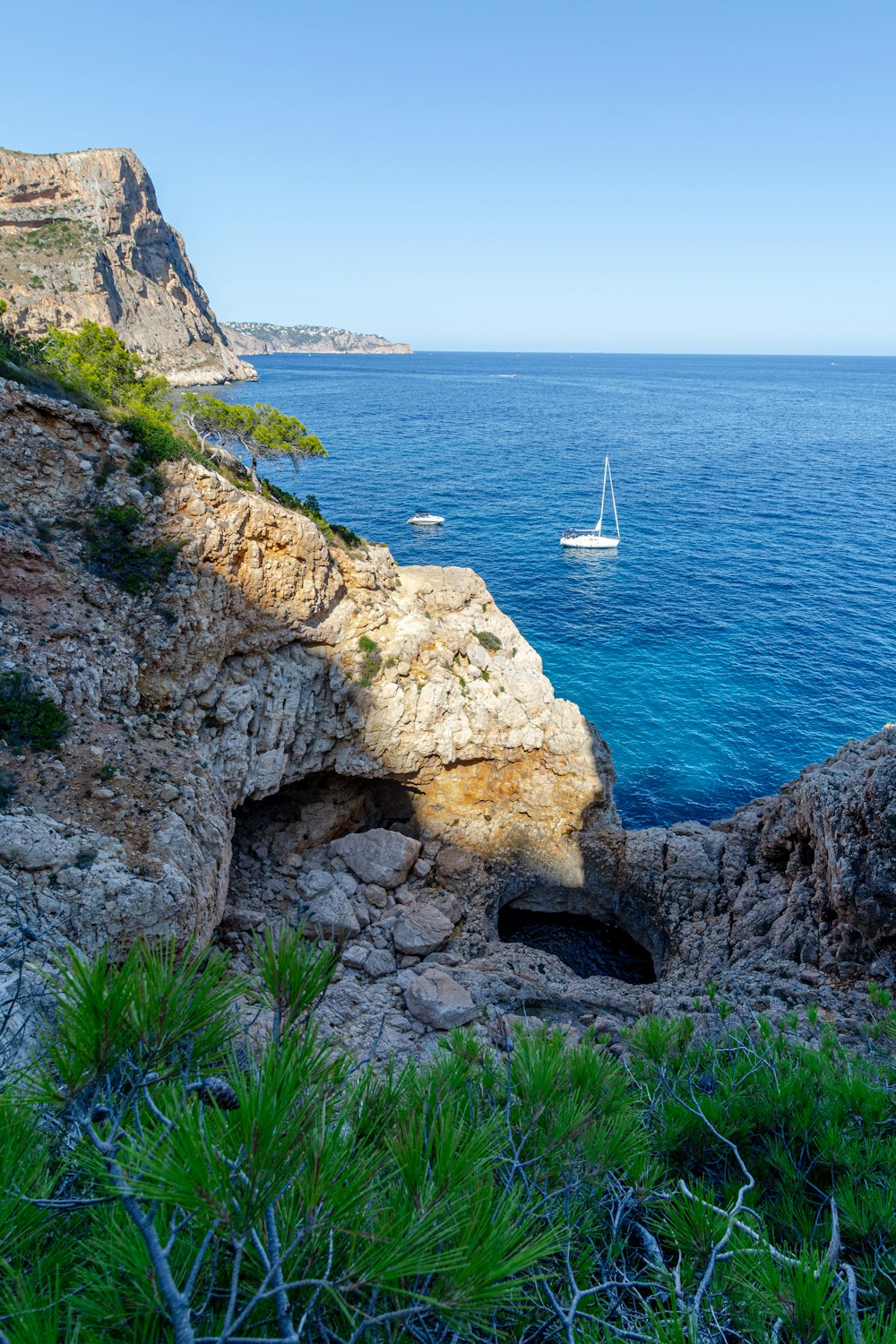 white sailboat on sea near brown rock formation during daytime