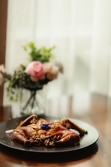 A close-up shot of a golden amber-hued roasted chicken resting on a cream-colored plate with sage green herbs sprinkled around.