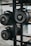 Several cylindrical fitness sandbags are stored on a black metal rack. The visible sandbags are labeled with different weights such as 20, 30, and 40 pounds and feature handles for easy carrying.