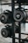 Several cylindrical fitness sandbags are stored on a black metal rack. The visible sandbags are labeled with different weights such as 20, 30, and 40 pounds and feature handles for easy carrying.