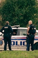 2 police men standing on white police car during daytime