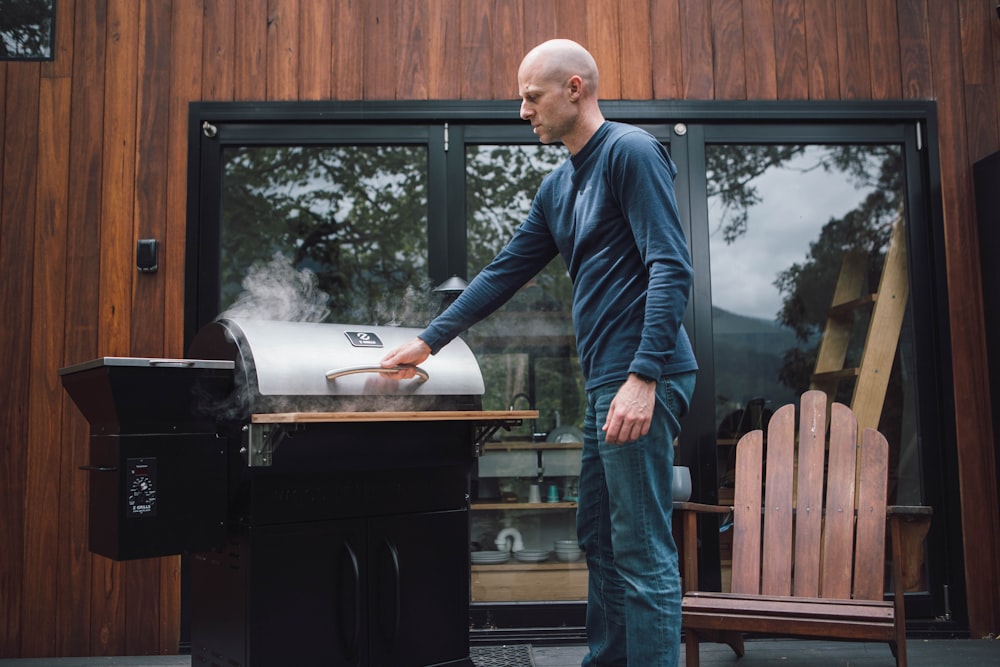 man in blue dress shirt and blue denim jeans standing beside brown wooden framed glass window