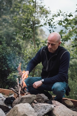 man in black long sleeve shirt and blue denim jeans sitting on brown log during daytime