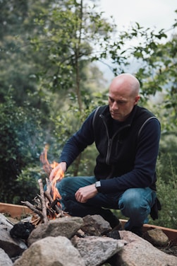 man in black long sleeve shirt and blue denim jeans sitting on brown log during daytime
