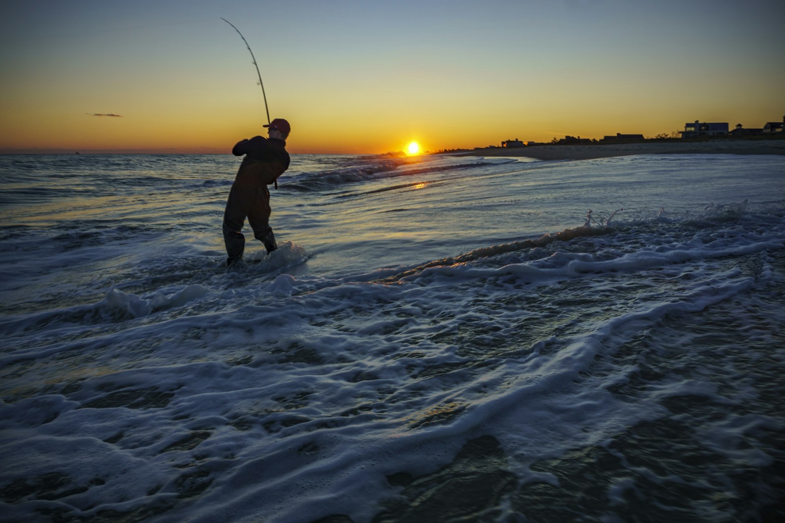 Silhouette of an angler surf fishing for striped bass at sunset