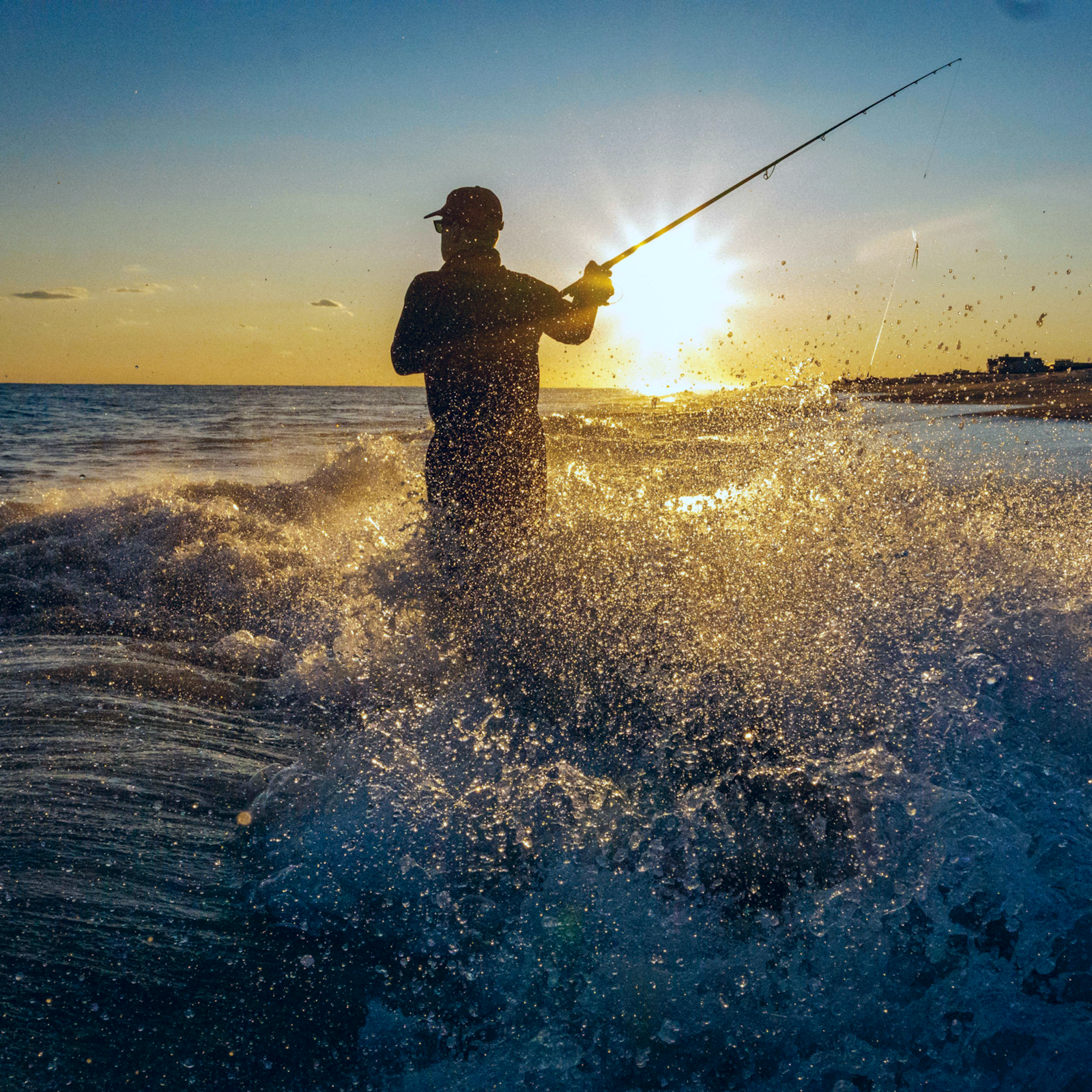 Surf fisherman silhouetted against ocean waves at sunset