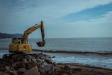 Skid steer loader maneuvering on a rocky construction site near the coast.