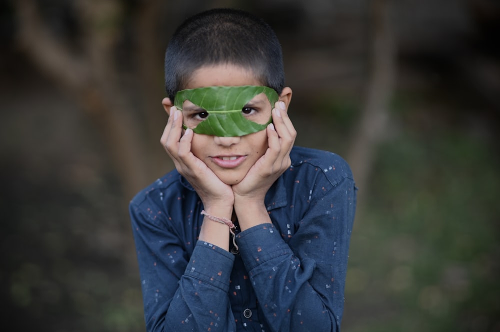 boy in blue dress shirt covering his face with green leaf