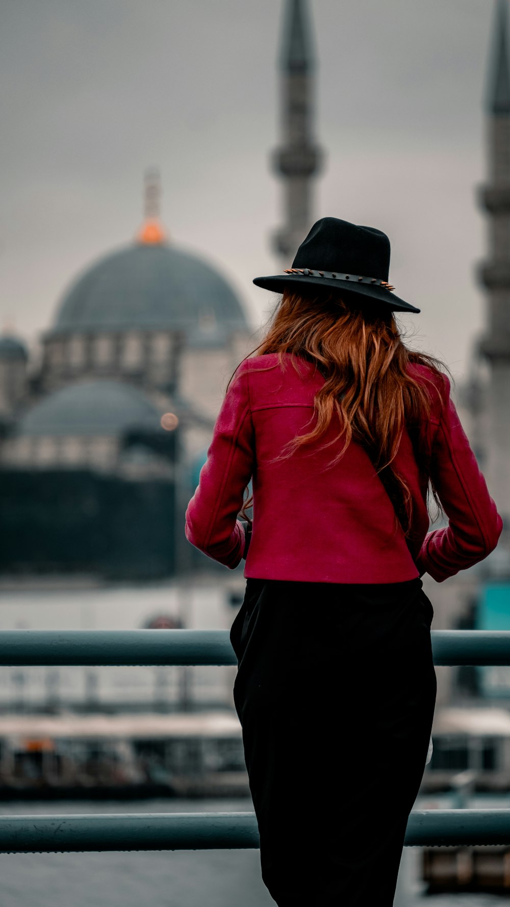 woman in red long sleeve shirt and black hat standing near blue metal railings during daytime