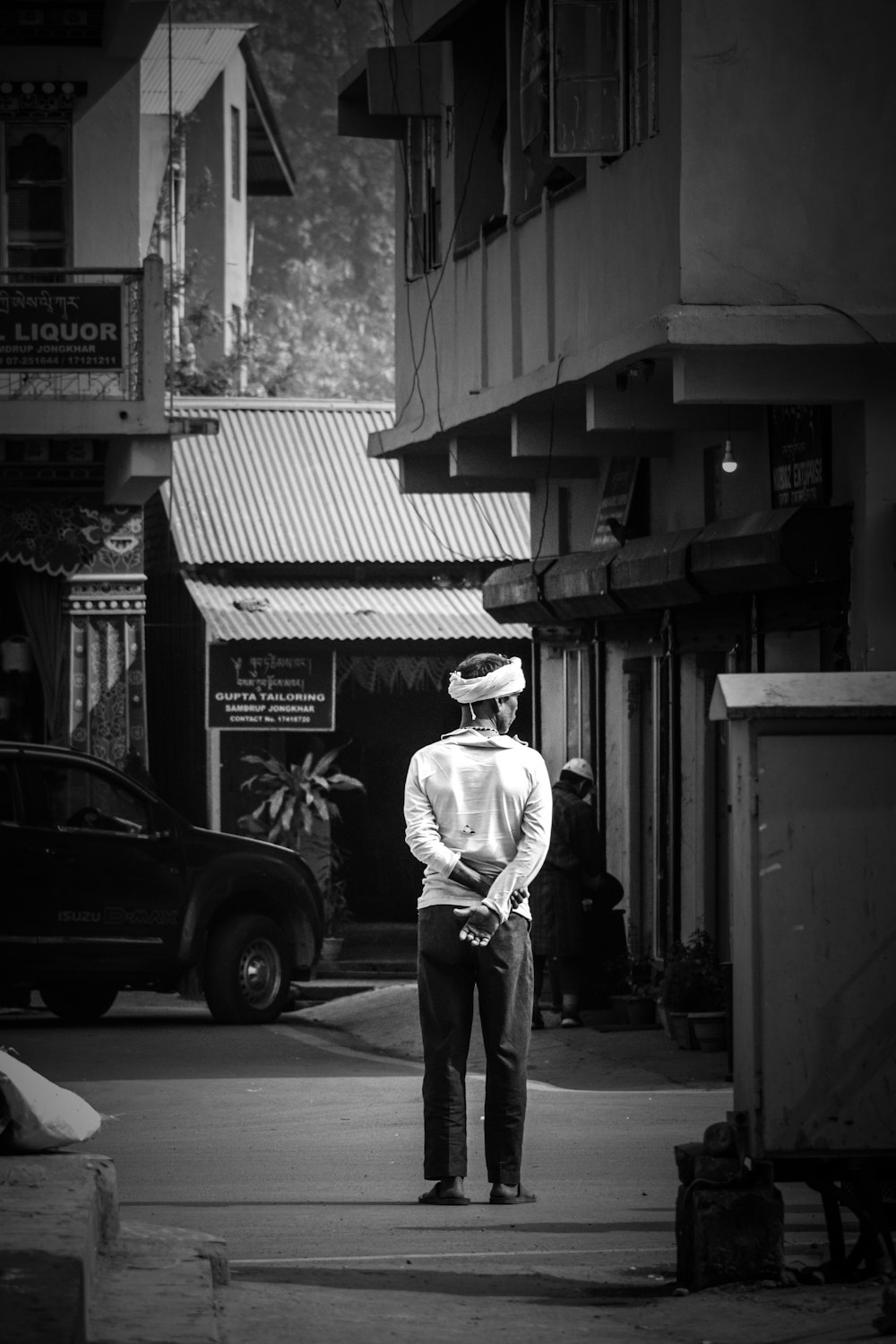 grayscale photo of man in hat and pants standing near car