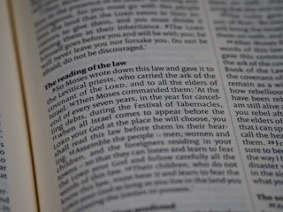A close-up view of a page from a religious text, featuring printed paragraphs with a bold heading 'The reading of the law'. The text discusses instructions given by Moses about laws and the Festival of Tabernacles. The words are neatly aligned in columns.